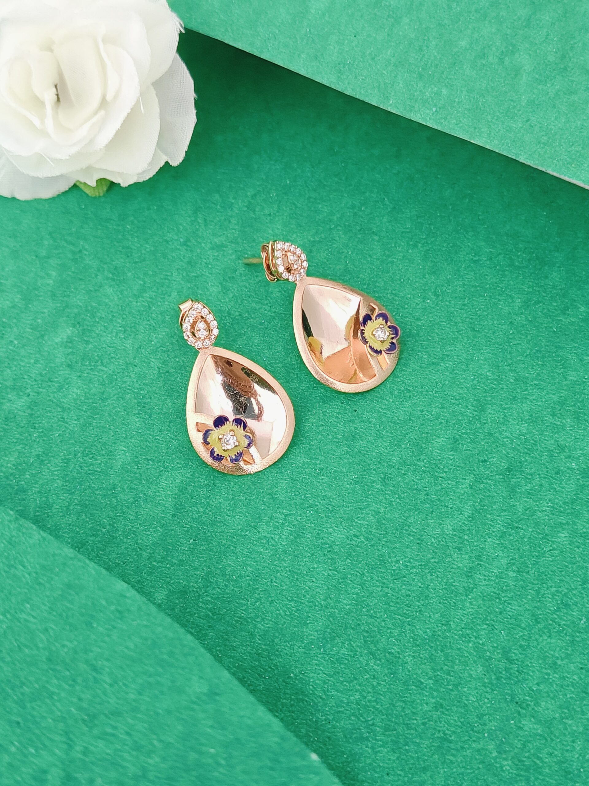 Rose gold teardrop earrings with floral details on a green surface with a white flower.
